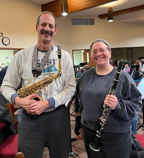 a tall man holding an alto saxophone, standing next to a woman in a gray sweatshirt, holding a clarinet