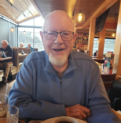 smiling man with a goatee, wearing glasses and a light blue jacket