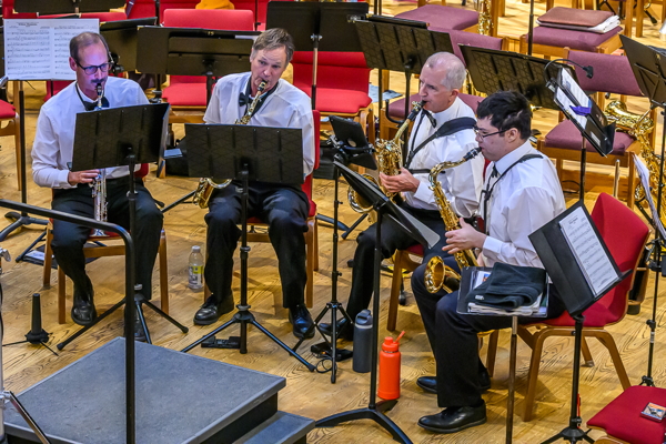four men, seated. They are wearing black pants, white shirts and black bow ties. From left to right, they are playing soprano, alto, baritone and tenor saxophones.